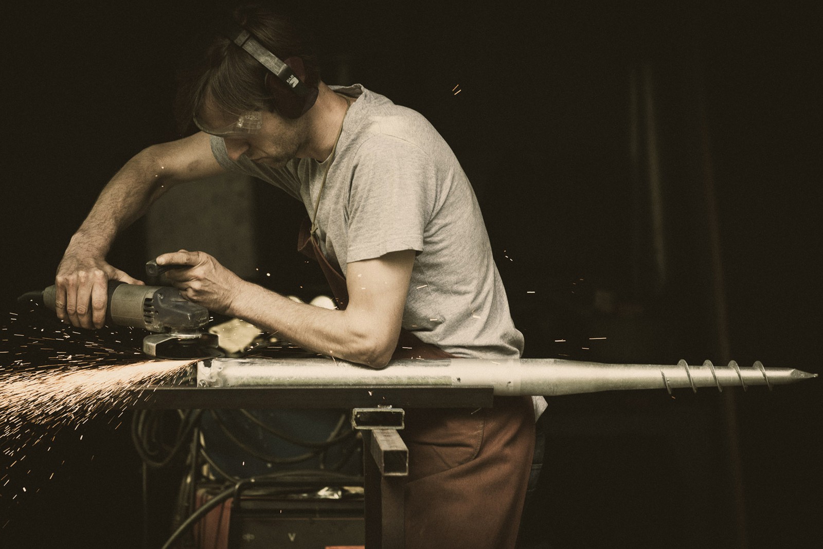 Black-and-white documentary photo of a craftsman manually working on a piece of wood at a workbench, showing the traditional manufacturing process of the Krimberg product, the screw table