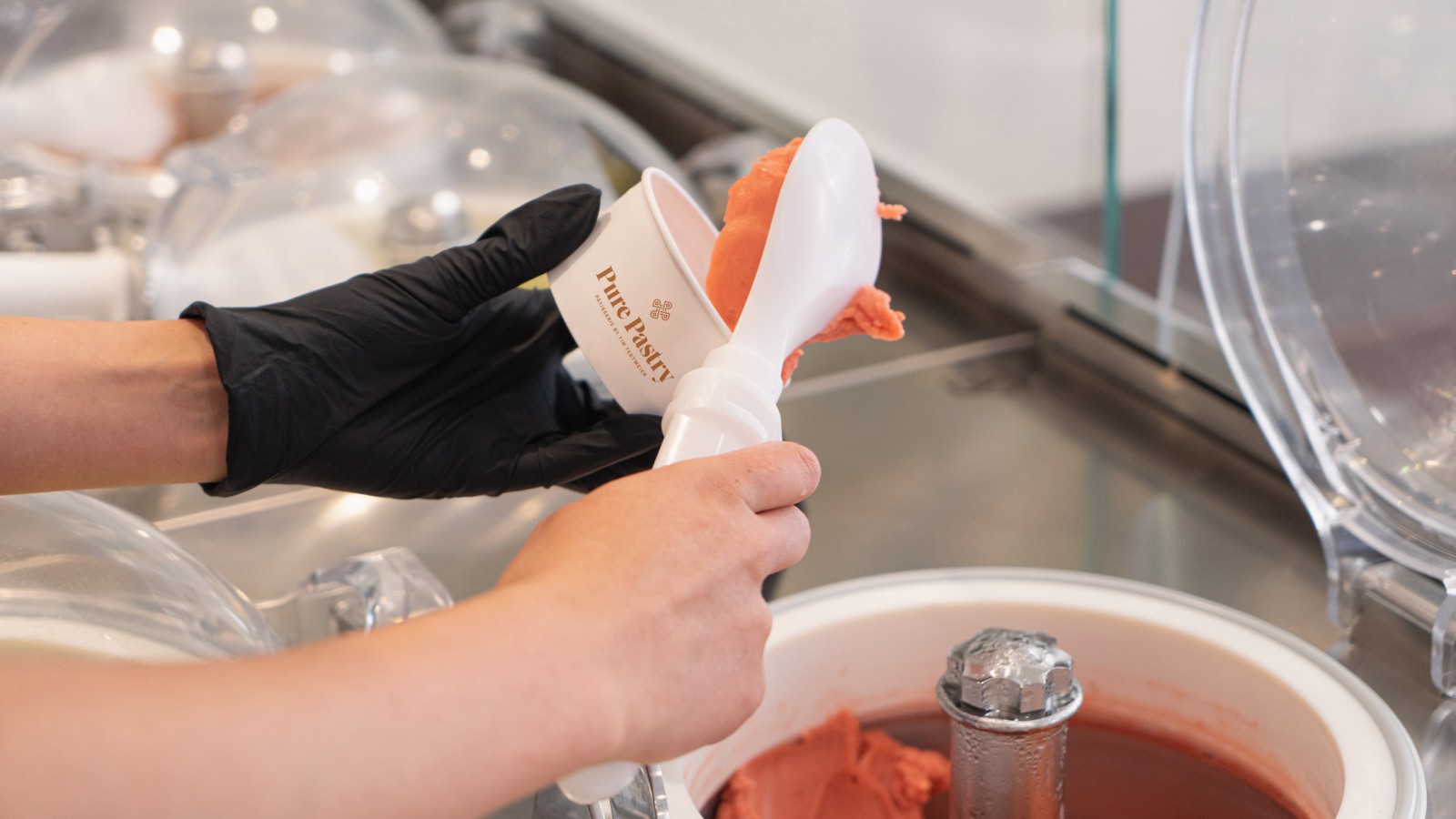 A pastry chef wearing black gloves fills a flambéed ice cream sundae with Pure Pastry's handmade ice cream