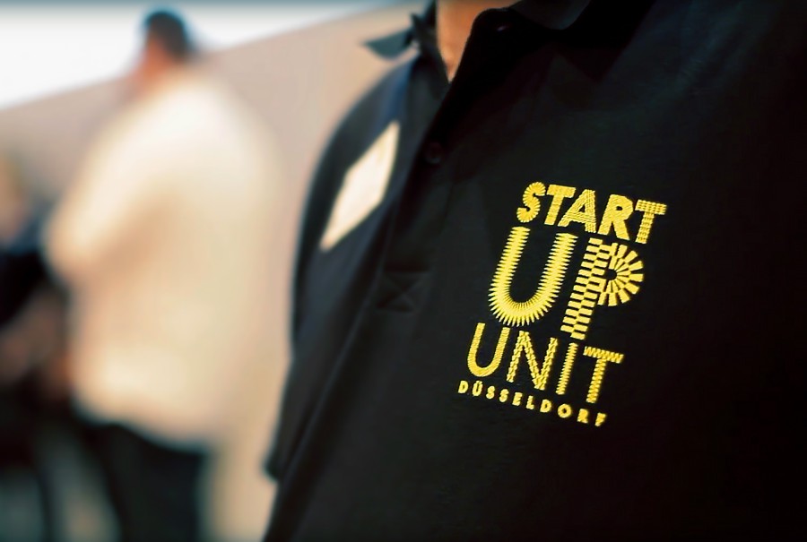 Close-up of a black shirt with the yellow “Startup Unit Düsseldorf” logo on the chest